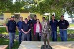 Smiling group of people pose behind a metal statue of a firefighter