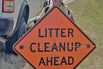 Photo of a smiling female BLM-NCMD employee holding a bright-orange sign reading "Litter Cleanup Ahead."