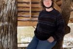 woman poses in a pavilion leaning against a wooden post