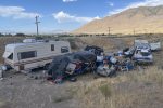 A camper and a vehicle are pictured among piles of debris and trash 
