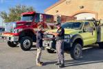Two men exchange keys in front of fire engines.