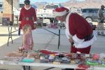 Mrs. Claus standing in the background watching a little girl visit with Santa Claus next to the table where children chose a present while visiting.