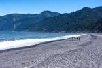 four hikers walk along beach near mountains and water on a blue bird day.