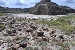 Rock-strewn desert landscape with a large, rounded rocky hill under a partly cloudy sky.