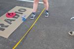 A young woman uses a tape measure in a black parking lot to paint parking lines