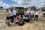 Group of young volunteers posing outdoors with collected plants and yard waste on a sunny day.