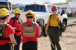 a wildland firefighter in yellow shirt, green pants, and hard hat, speaks to high school students
