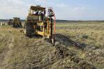 Three tractors using specialty plows bury power and fiber optic cable lines across a prairie landscape.