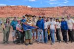 a group of people with an antelope mascot stand in front of distant red-rock cliffs