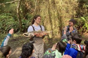 A volunteer holds a large salmon in front of a group of children.