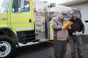 Two men review a document while standing in front of a water truck.