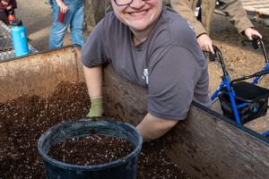 A smiling woman in a gray shirt puts potting soil into a pot. 