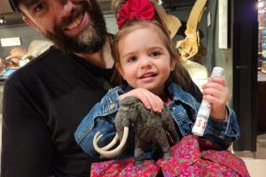 Man in black shirt holds young girl who holds a small stuff wooly mammoth