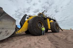 Person in a white hard hat and neon yellow safety vest pointing towards a rocky cliff face at a mining or excavation site.
