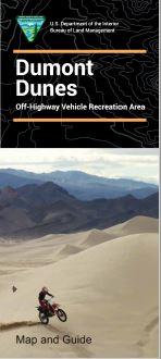 Dirt Bike rides up a series of dunes with mountains in the background.