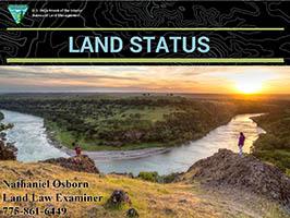 At the top of the screen, the words "Land Status" appear on a black background with white topographical lines. Most of the screen is taken up by a photo of two hikers in red jackets overlooking a bend in a river with the sun setting in the distance.