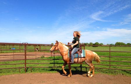 Girl riding horse along fence line.