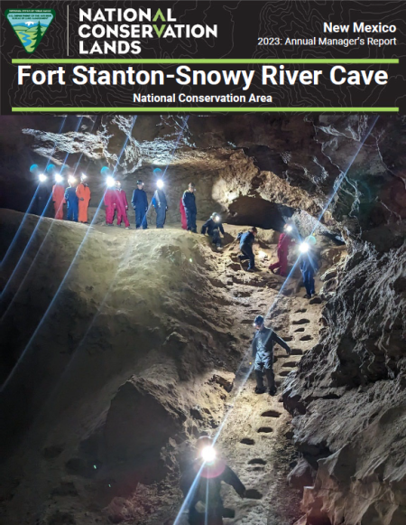 line of people hiking down stone steps of dark cave illuminating area with headlamps
