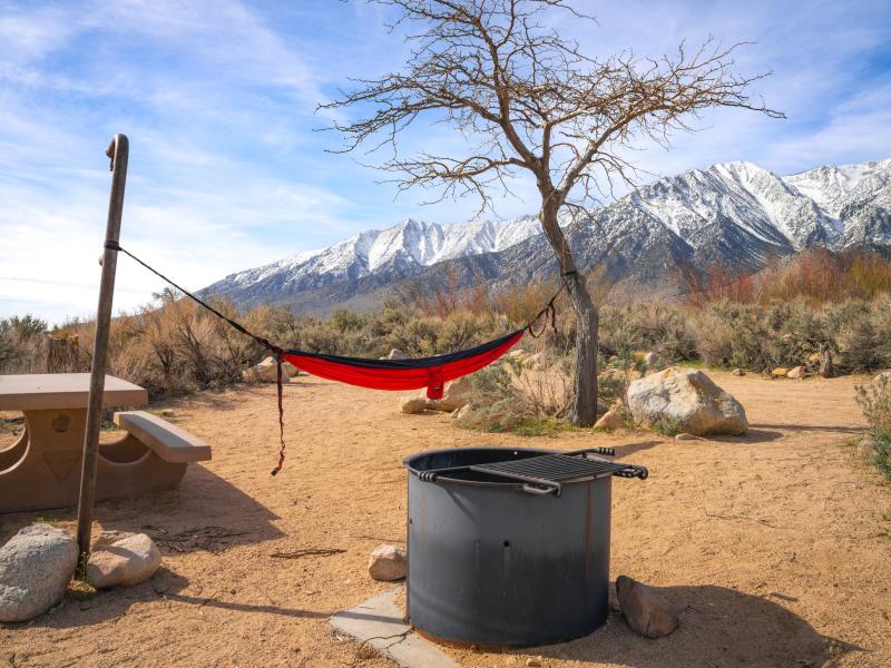 desery campground with a fire pit and hammock and snow capped mountains in the distance