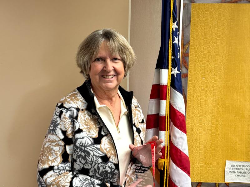 Ramona Daniels stands with award near an american flag.