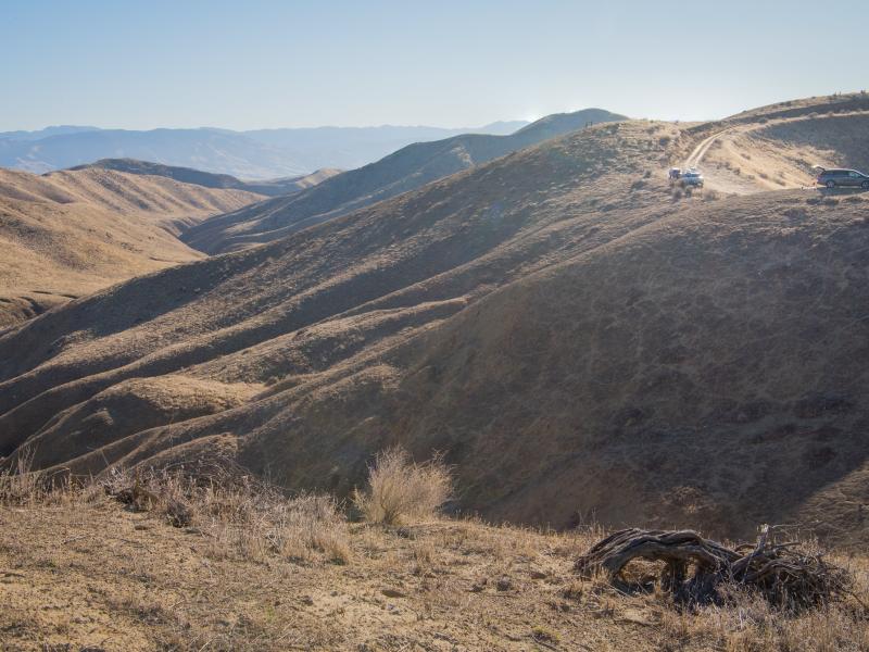 tan hills and cars driving on a dusty road.