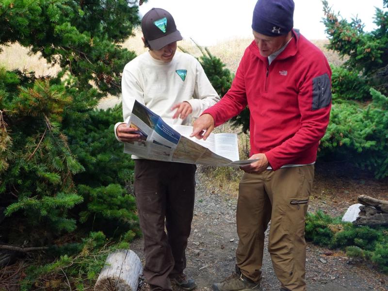 a red fleece man looks at a map with another white shirt man