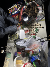 Hands arranging pinecones and Scrabble tiles on a cluttered table illuminated by a lantern at night.