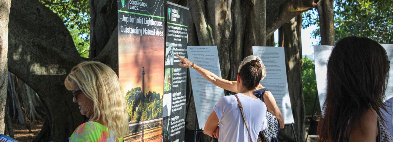 People viewing large posterboards with BLM and Jupiter Inlet Lighthouse Outstanding Natural Area info during an open house at the ONA